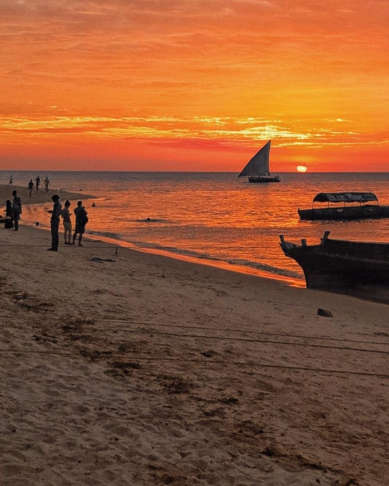 Sunset over a white sand beach in Zanzibar, Tanzania, with traditional dhow boats