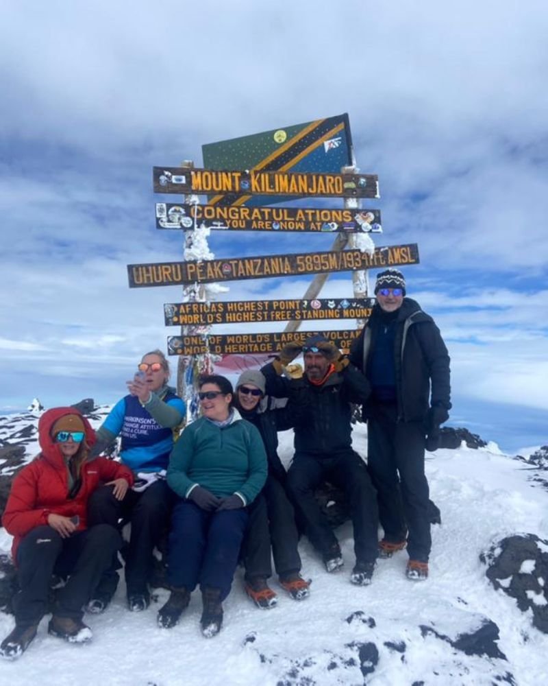 Climbers celebrating at the Uhuru Peak summit sign on Mount Kilimanjaro, Tanzania after reaching Africa's highest point